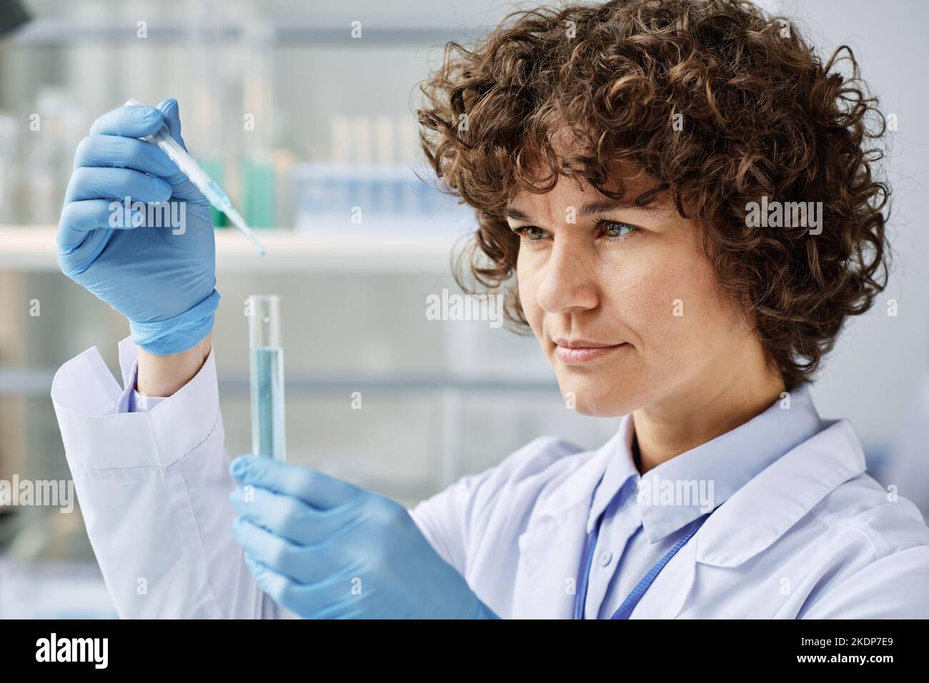 Young clinical expert in labcoat adding drop of liquid substance to another one during work over new scientific research Stock Photo