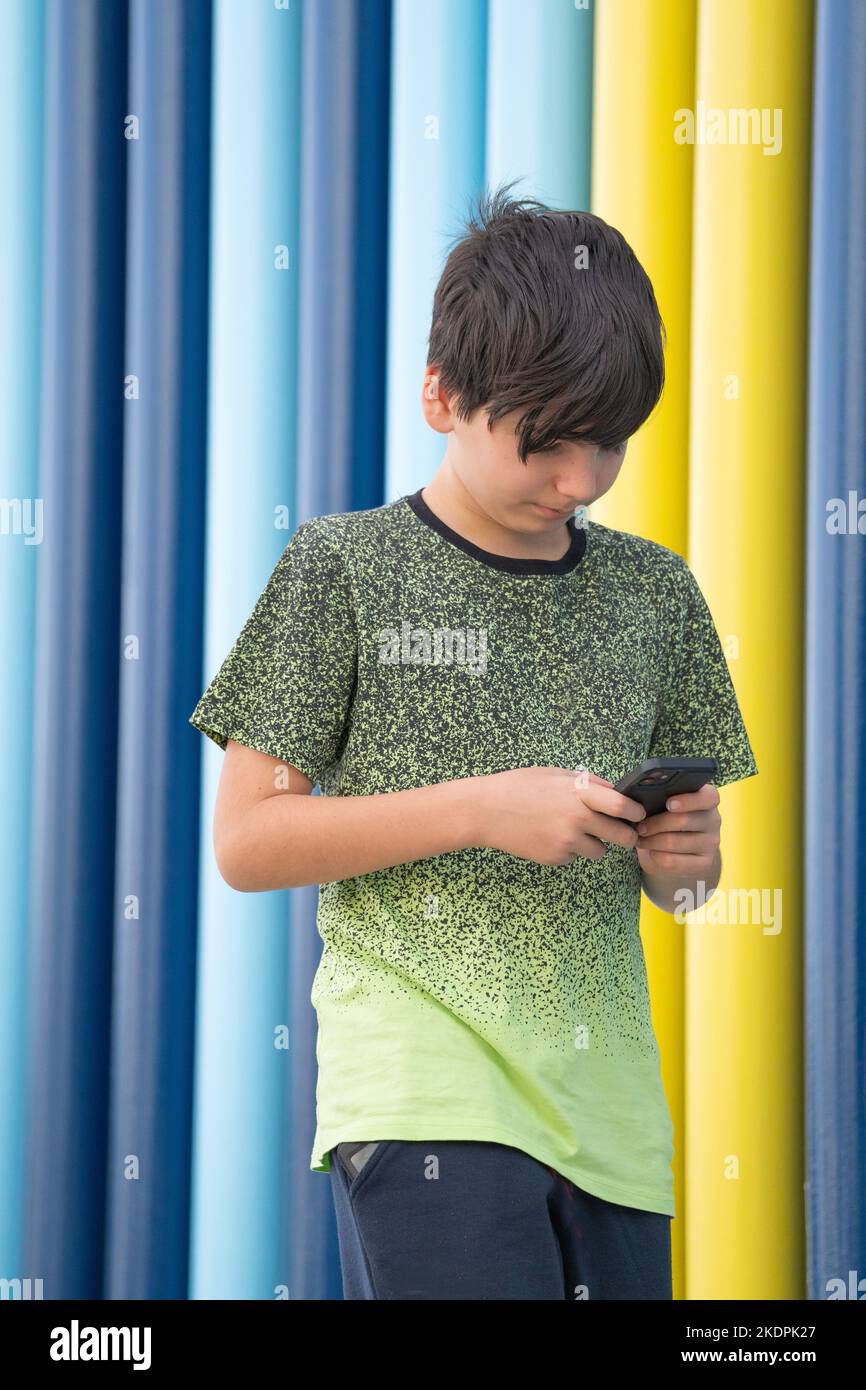 Portrait of a young boy using a smartphone walking on coloured background. Immersed in technology concept. Stock Photo