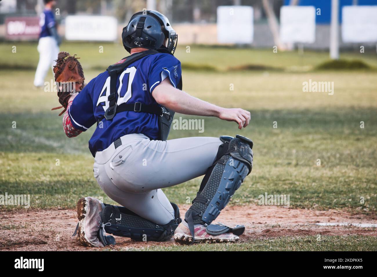 A baseball catcher holding up a leather glove on one knee on the pitch