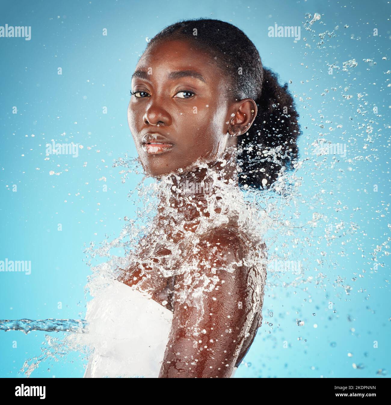 Splash, water and portrait of black woman for beauty, care of body and wellness against blue studio background. Health, skincare and African girl Stock Photo