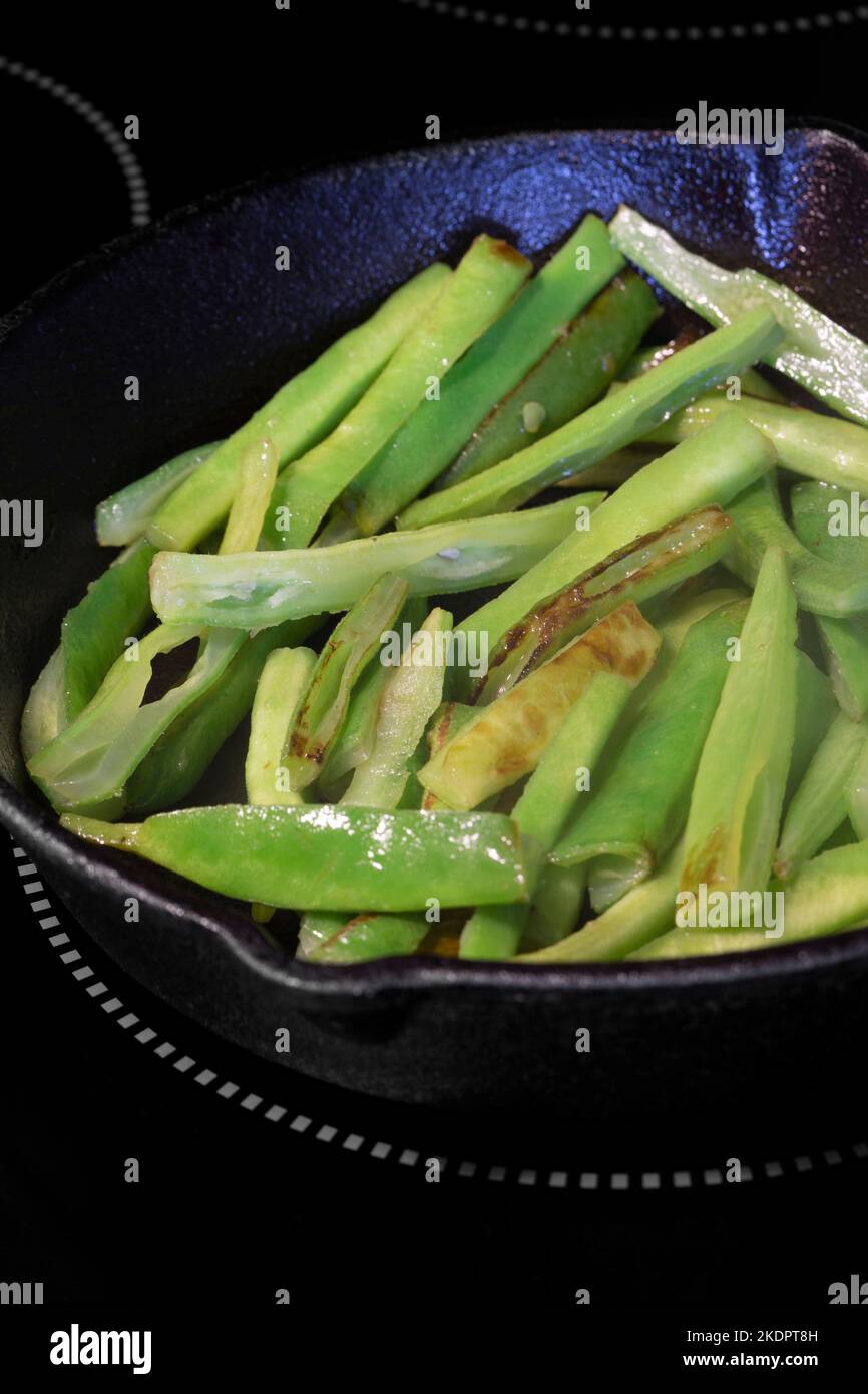 Frying green beans, with olive oil, in a cast iron frying pan, on an electric hob stove. Stock Photo