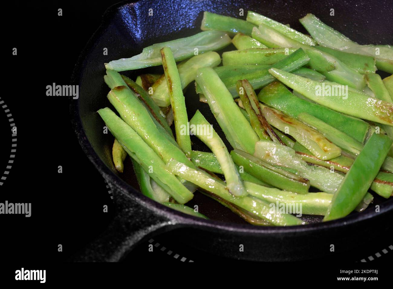 Frying green beans, with olive oil, in a cast iron frying pan, on an electric hob stove. Stock Photo