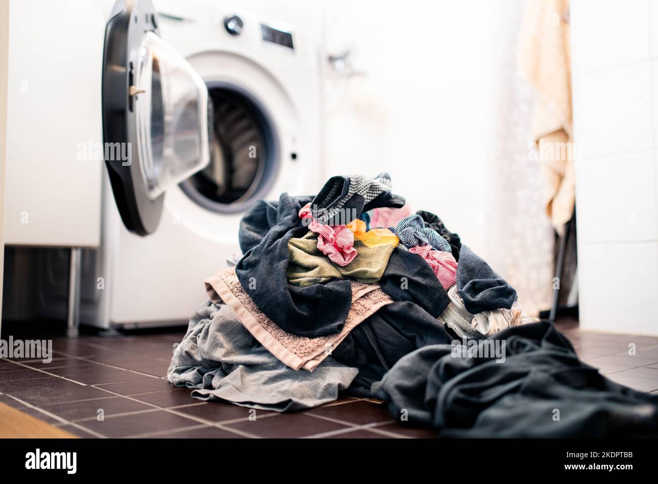Laundry day. Washing machine in the background, pile of dirty clothes on the floor. Family house chores and domestic work concept. Heap of socks. Stock Photo
