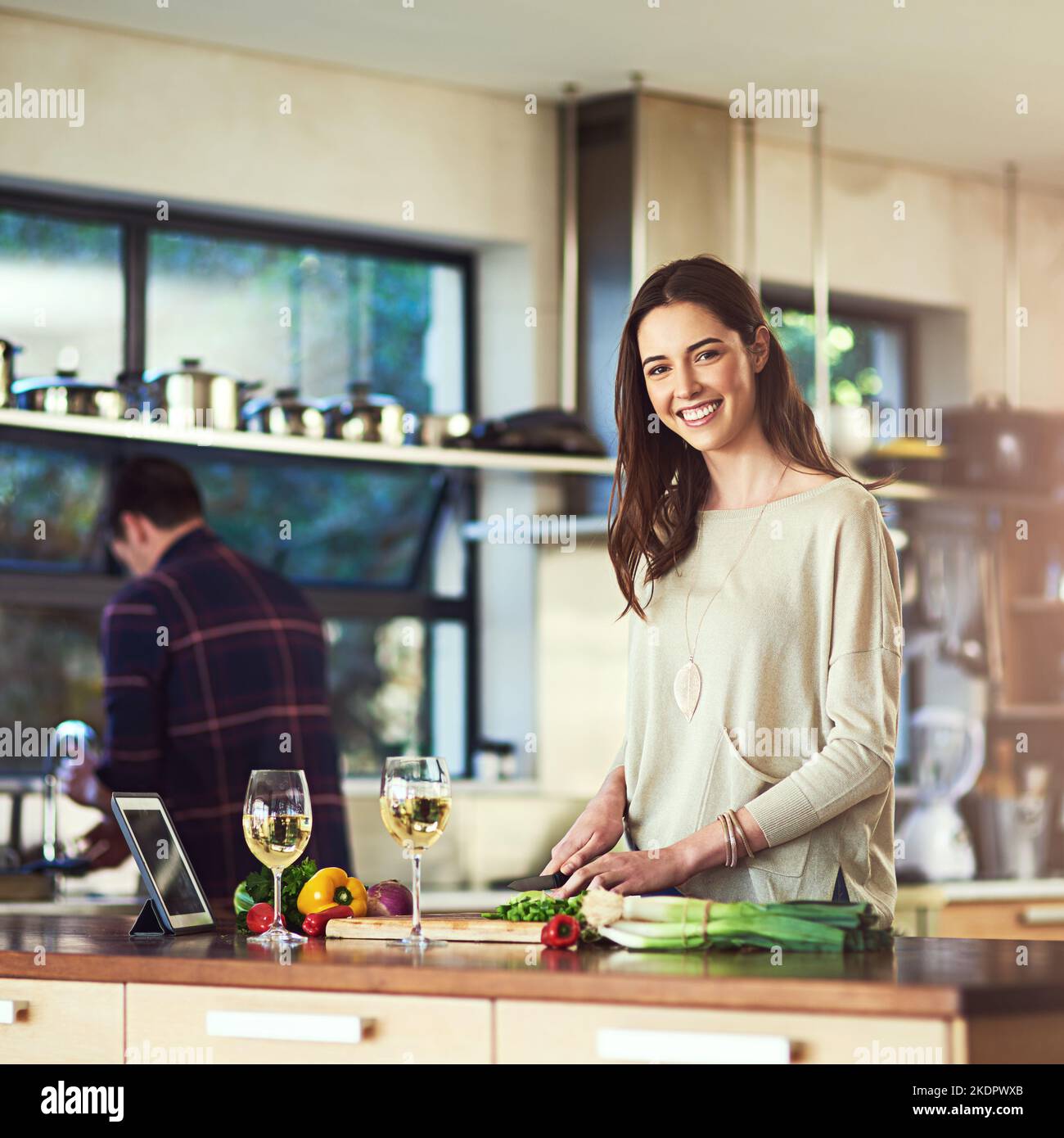 Nothing better than a hearty home cooked meal. Portrait of a young woman preparing a meal with her boyfriend in the background at home. Stock Photo