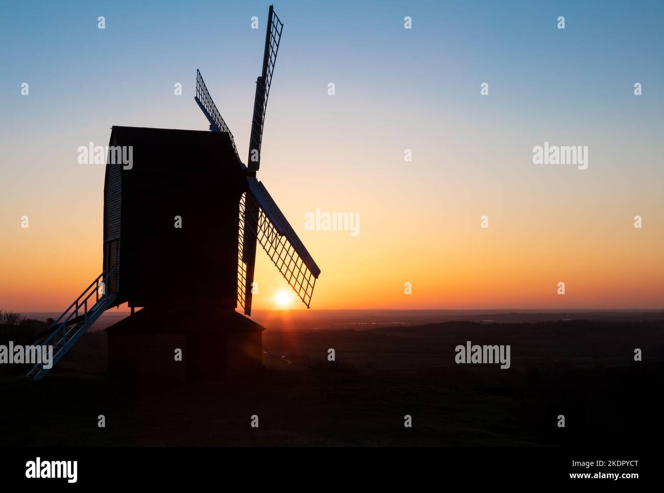 Sun setting on the horizon behind a traditional wooden British windmill at sunset Stock Photo