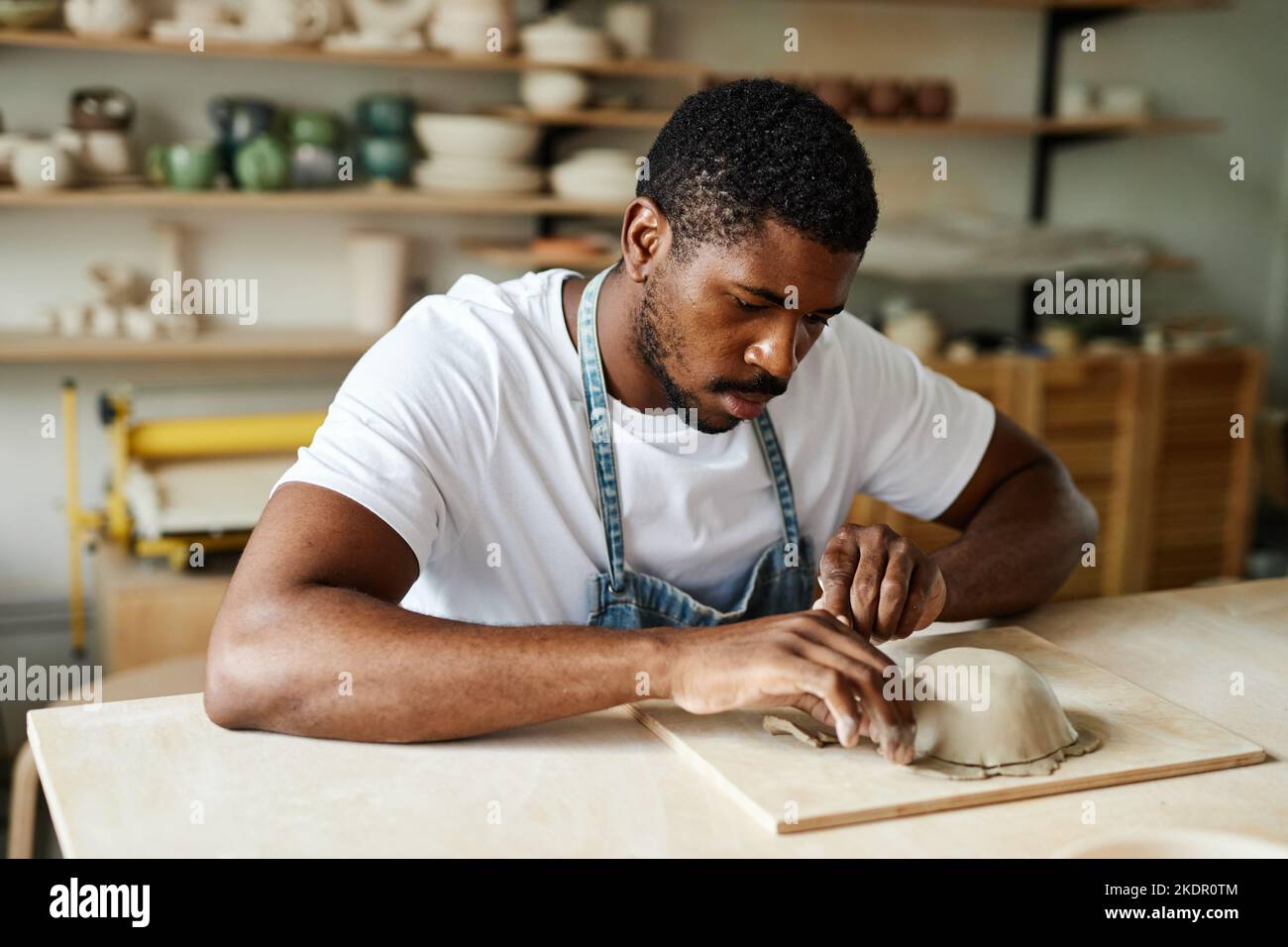 Warm toned portrait of creative black man shaping ceramic bowl in cozy