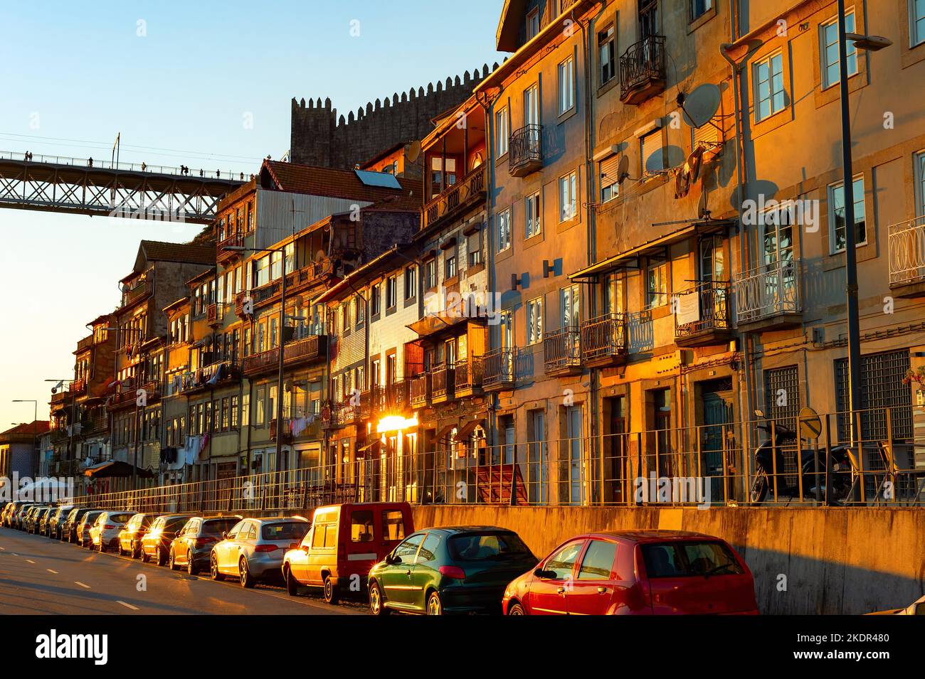 Sunset light reflects on fcades of traditional houses, parked cars, Dom Luis bridge, cityscape Porto, Portugal Stock Photo