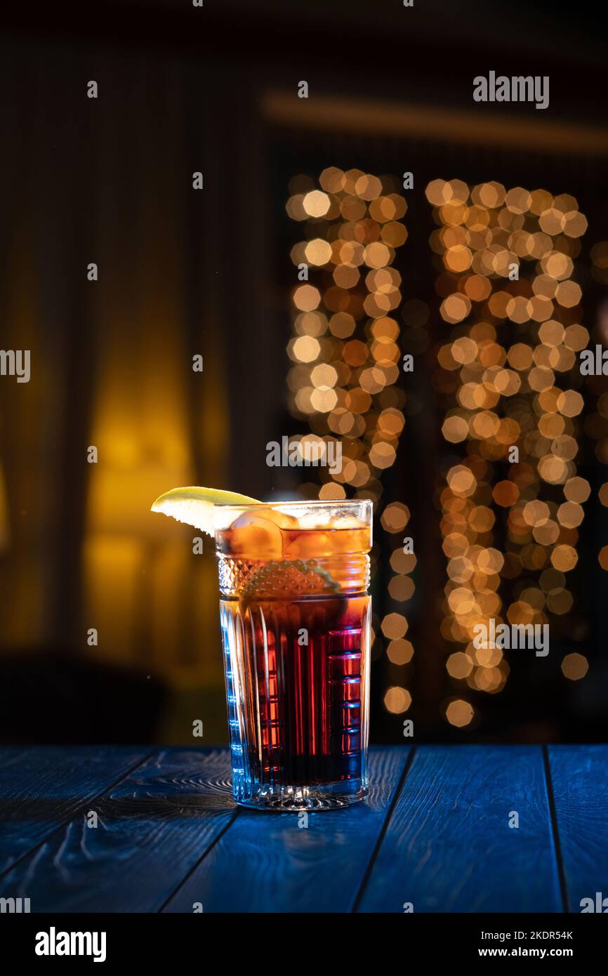 Glass of cocktail in bar on bright blurred background. Alcoholic cocktail with Coca-Cola, decorated lemon. Stock Photo