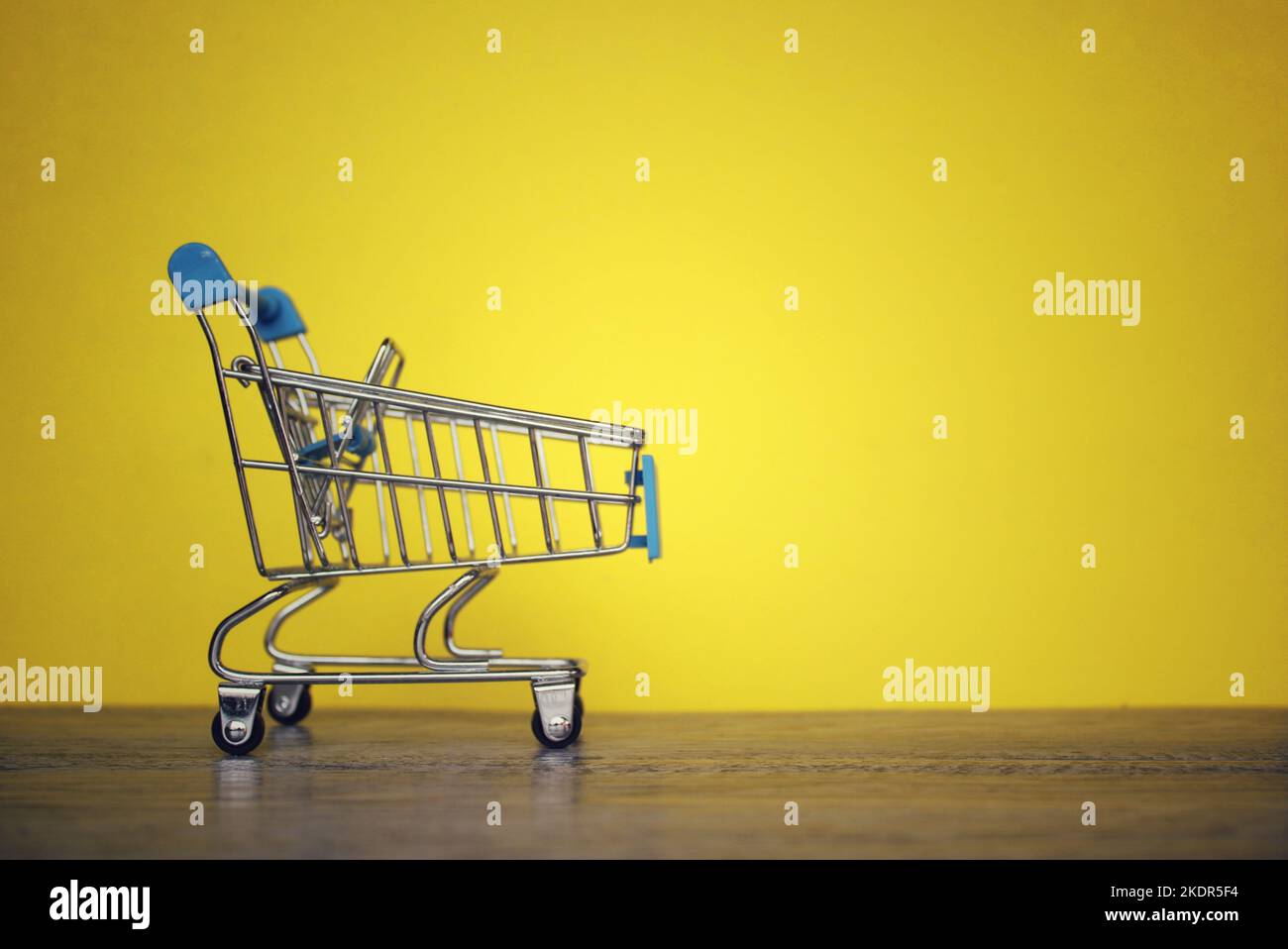 Mini shopping trolley on yellow background with copy space. Shopping and consumer concept. Stock Photo