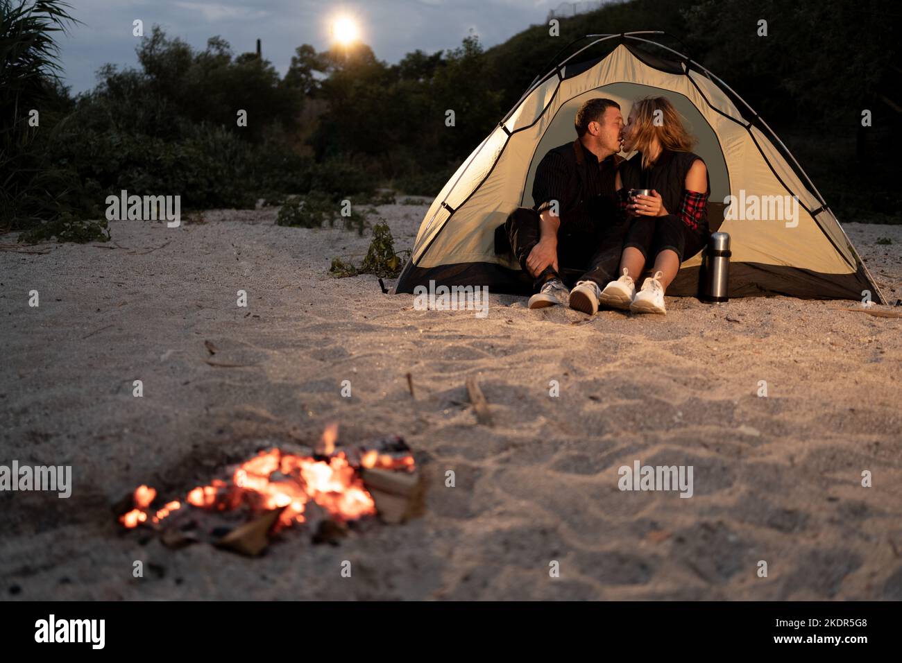 romantic couple on camping on sea shore of evening starry sky. Tourist couple, man and woman hikers sitting at bonfire Stock Photo