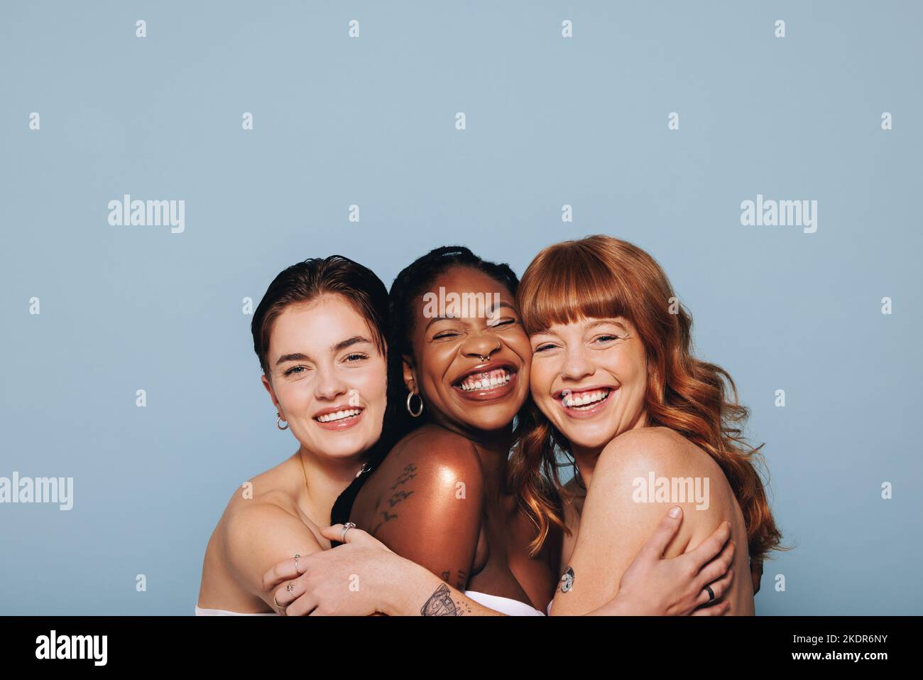 Three happy women with different skin tones smiling and embracing each other in a studio. Group of diverse women feeling comfortable in their natural Stock Photo