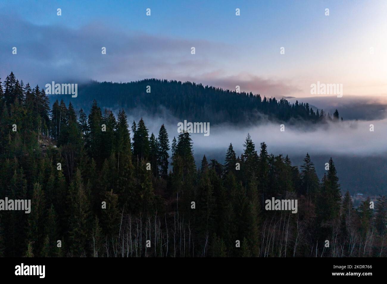 Mountain atmospheric landscape of high mountains in thick fog in rainy weather, panorama of mountain tops in thick clouds, dawn in the mountains in ea Stock Photo
