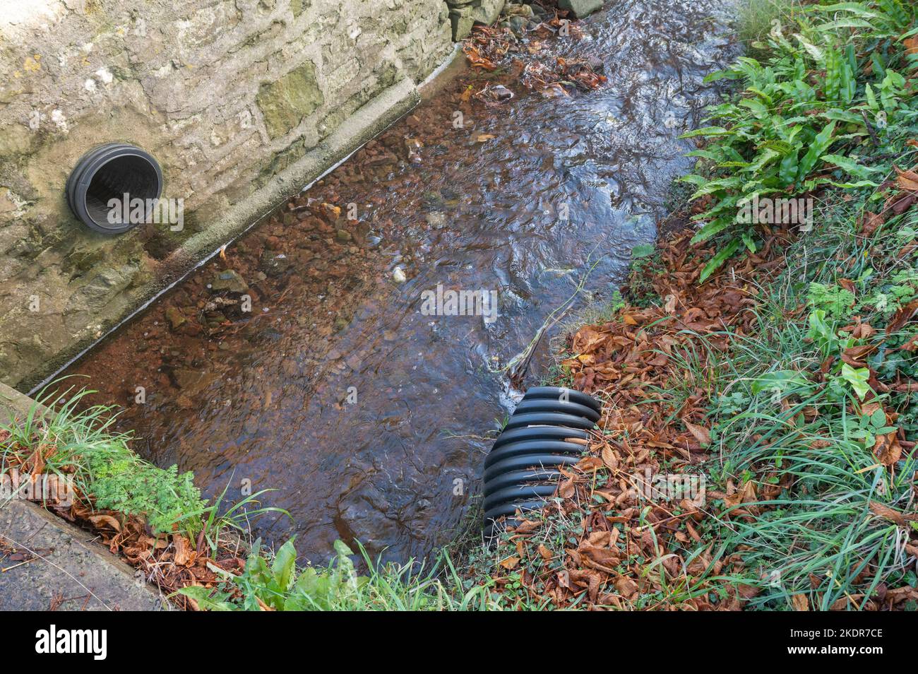 Black pipes drain surface water from a road into a stream Stock Photo