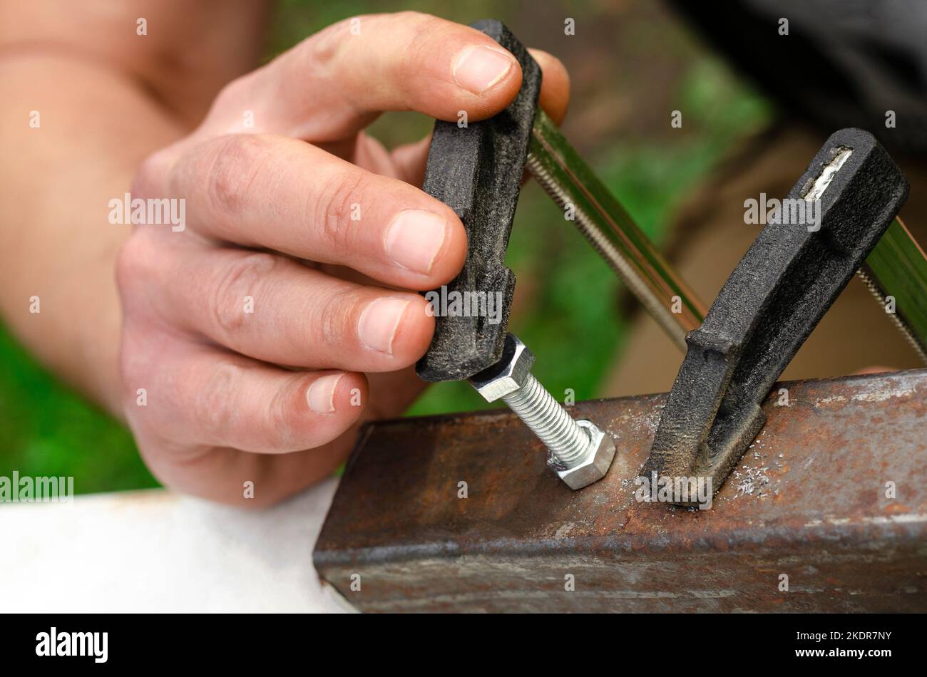 A man's hand screws a bolt into a metal nut. Working with metal Stock Photo