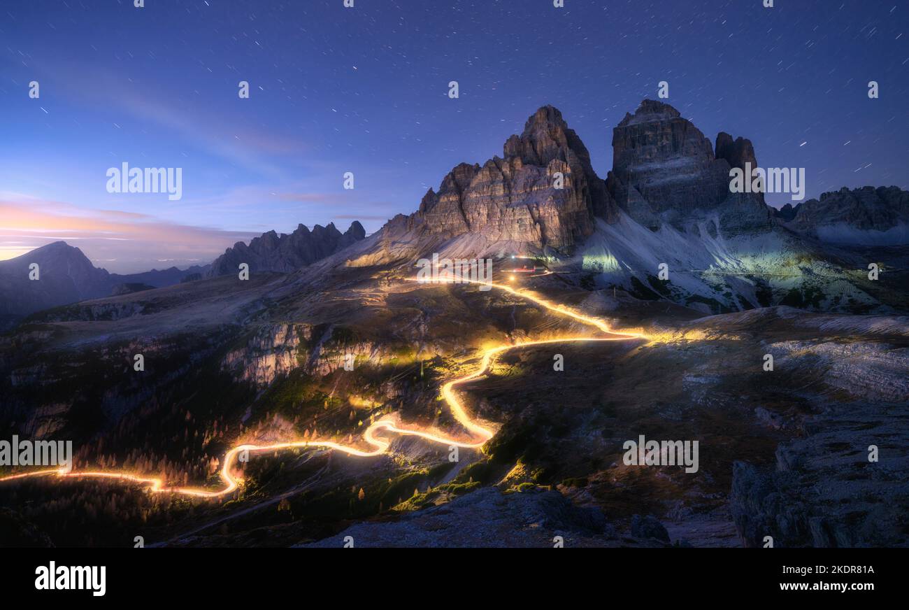 Car light trails on mountain road and high rocks at night Stock Photo