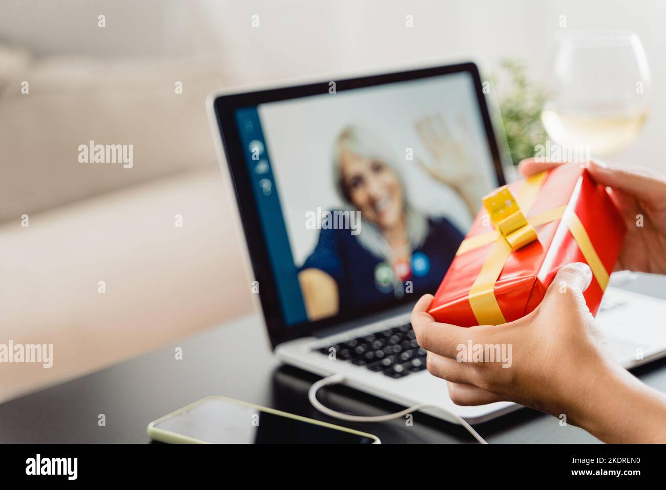 Young woman celebrating with grand mother in video call meeting during Christmas time - Focus on hand holding gift Stock Photo