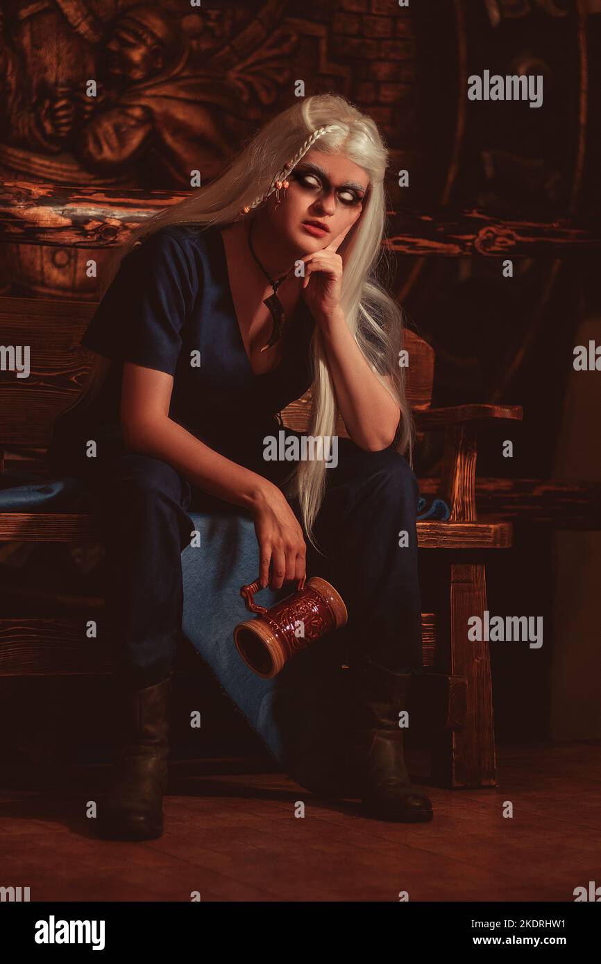 Viking woman with a mug in traditional warrior clothes inside a pub. Stock Photo