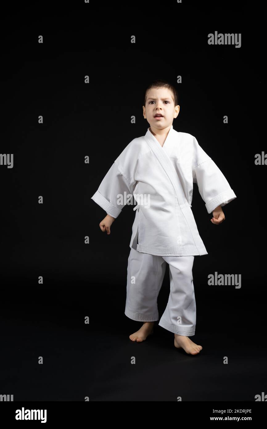 A little boy in a kimono practices karate on a black background