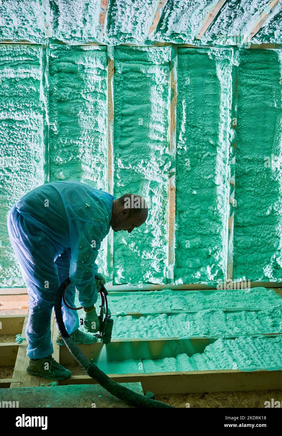 Male builder insulating wooden frame house. Man worker spraying polyurethane foam inside of