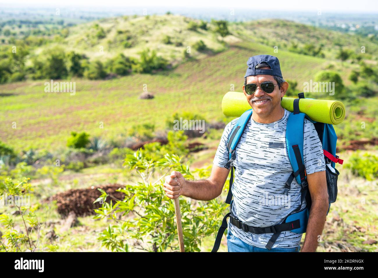 Portrait shot of Smiling middle aged hiker with backpack climbing mountain by looking at camera - concept of confidence, trekking and freedom Stock Photo