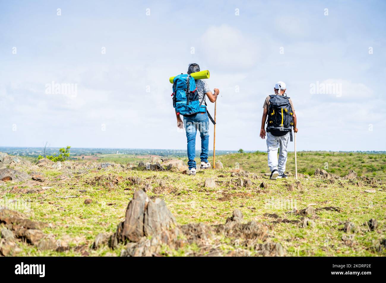 Back view tracking shot of middle aged hikers looking around after reaching destination on top of mountain - concept of achievement, trekking and Stock Photo
