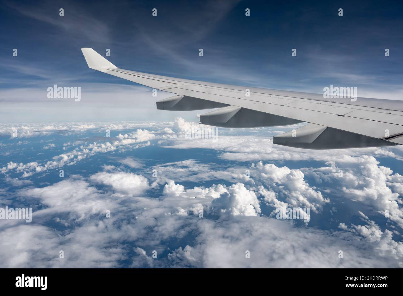 Wing of airplane above flat fluffy clouds surface with soft evening sunlight. Copy space. Stock Photo