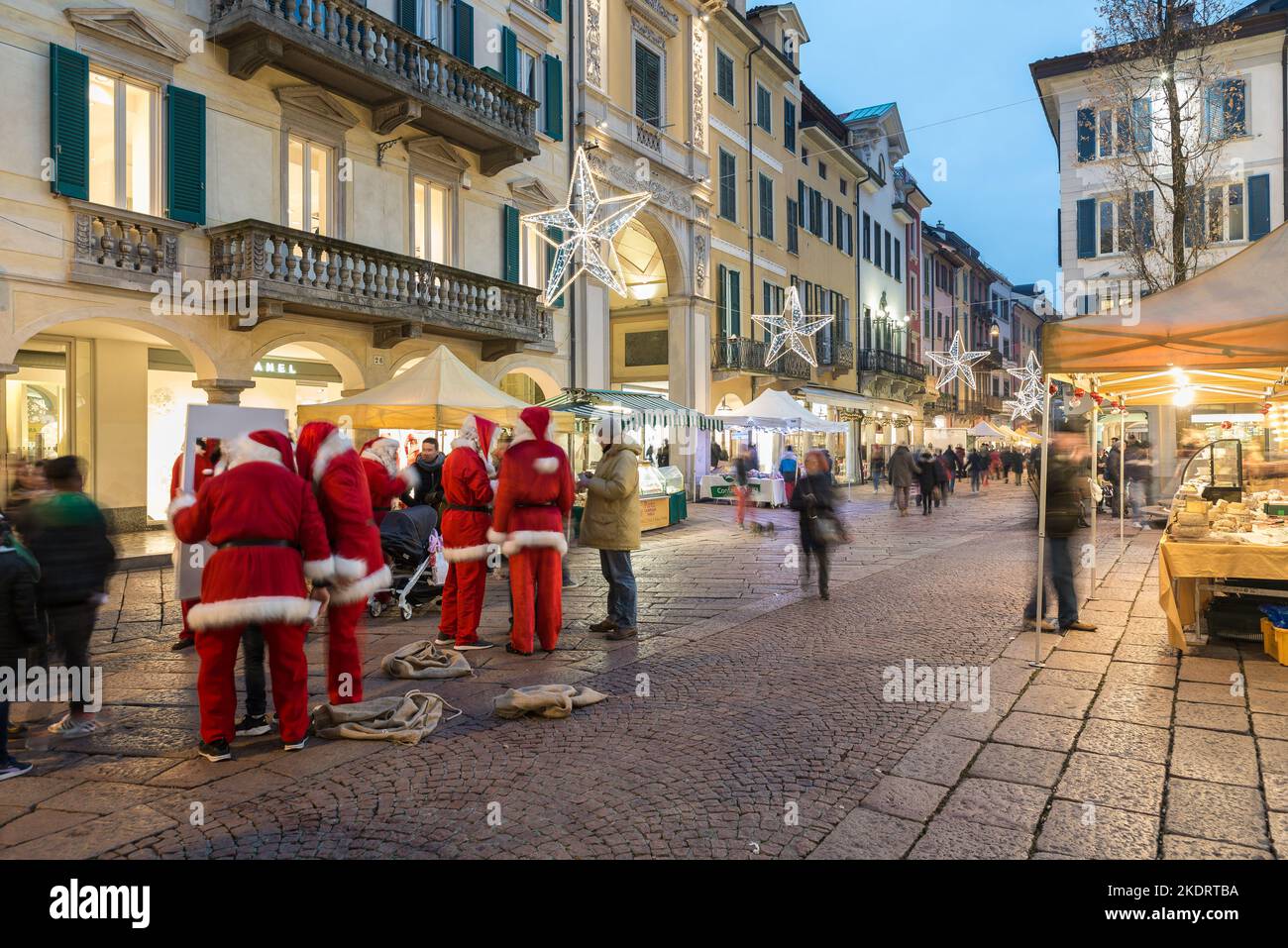 Christmas market at dusk and crowd of people on the street of a city with christmas lights. Historic center of Varese Stock Photo
