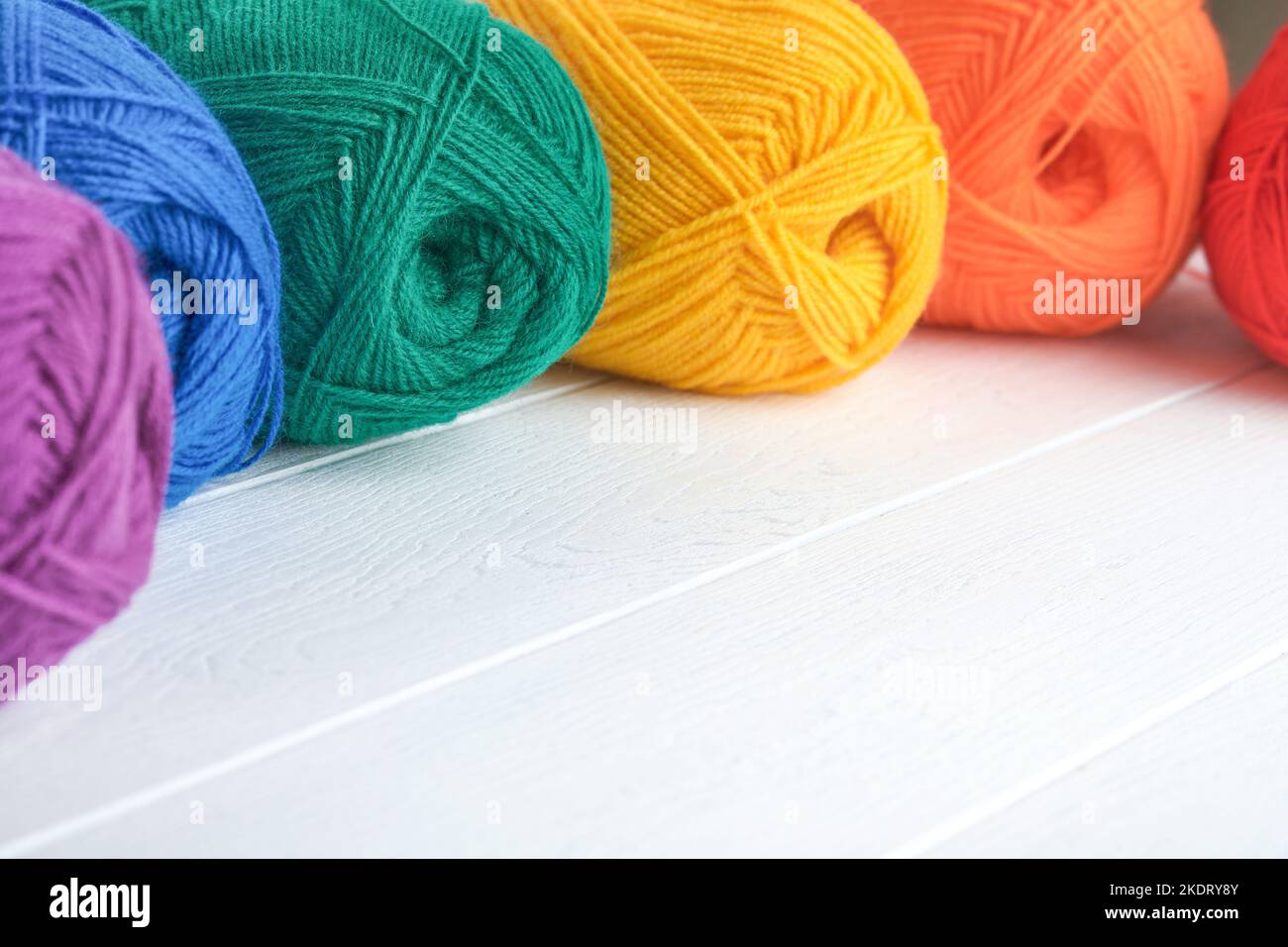 Many multi-colored balls of threads on knitted fabric on white wooden ...