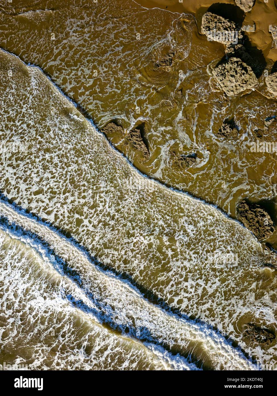 Top down aerial view of waves breaking onto a sandy beach with large boulders (Southerndown, Wales) Stock Photo
