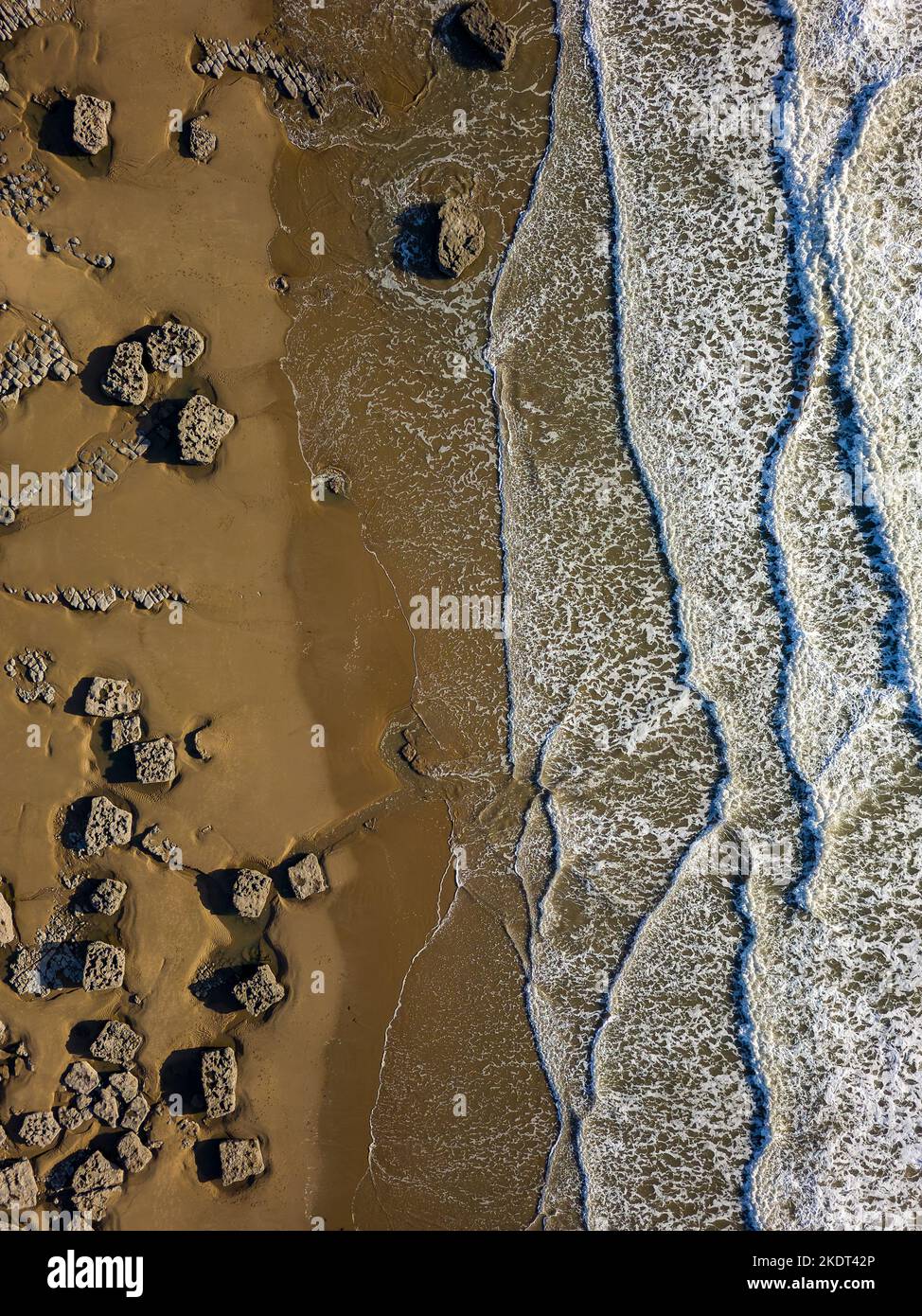 Top down aerial view of waves breaking onto a sandy beach with large boulders (Southerndown, Wales) Stock Photo