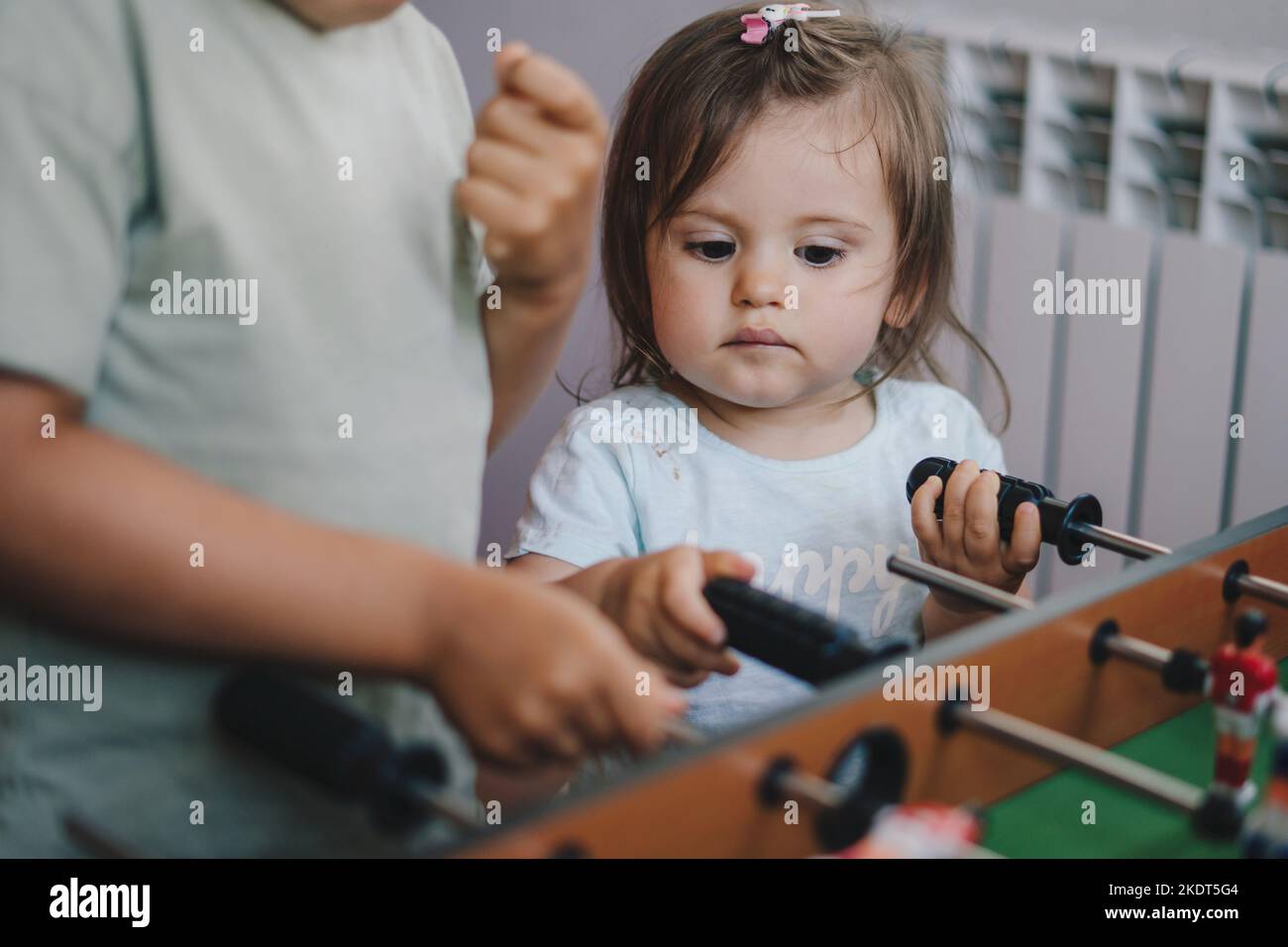 Baby's younger sister watching with admiration how her brother playing table football. Teamwork concept. Football concept. Children development Stock Photo