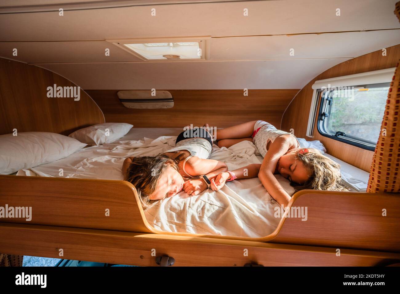 Kids are sleeping in alcove motorhome on road trip vacations. Children are resting in camper parked on a campsite in Greece with morning sunshine shin Stock Photo