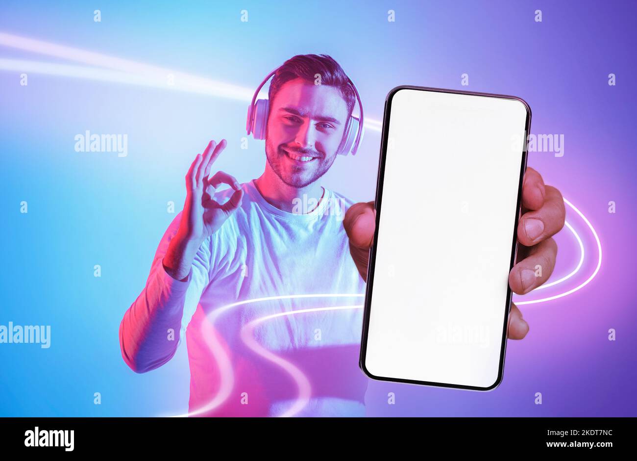 Handsome young man with headphones showing cell phone and okay Stock Photo