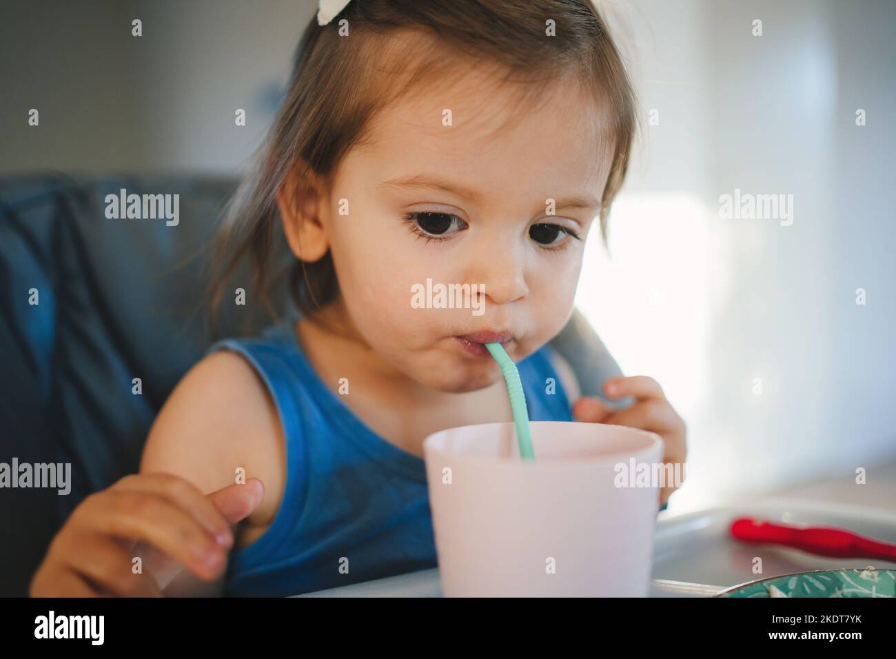 https://c8.alamy.com/comp/2KDT7YK/cheerful-little-baby-girl-drinking-milk-from-the-glass-with-straw-sitting-indoors-in-high-she-is-holding-the-plastic-glass-2KDT7YK.jpg