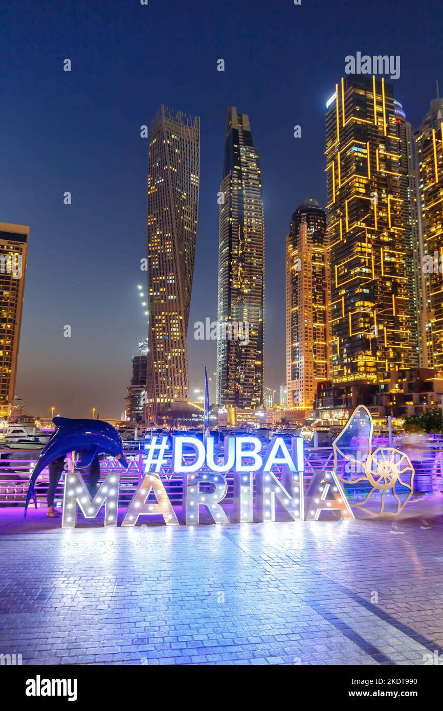 Dubai, United Arab Emirates - May 24, 2021: Dubai Marina Logo And Harbour Skyline Architecture Luxury Vacation In Arabia With Boat Yacht At Night Port Stock Photo