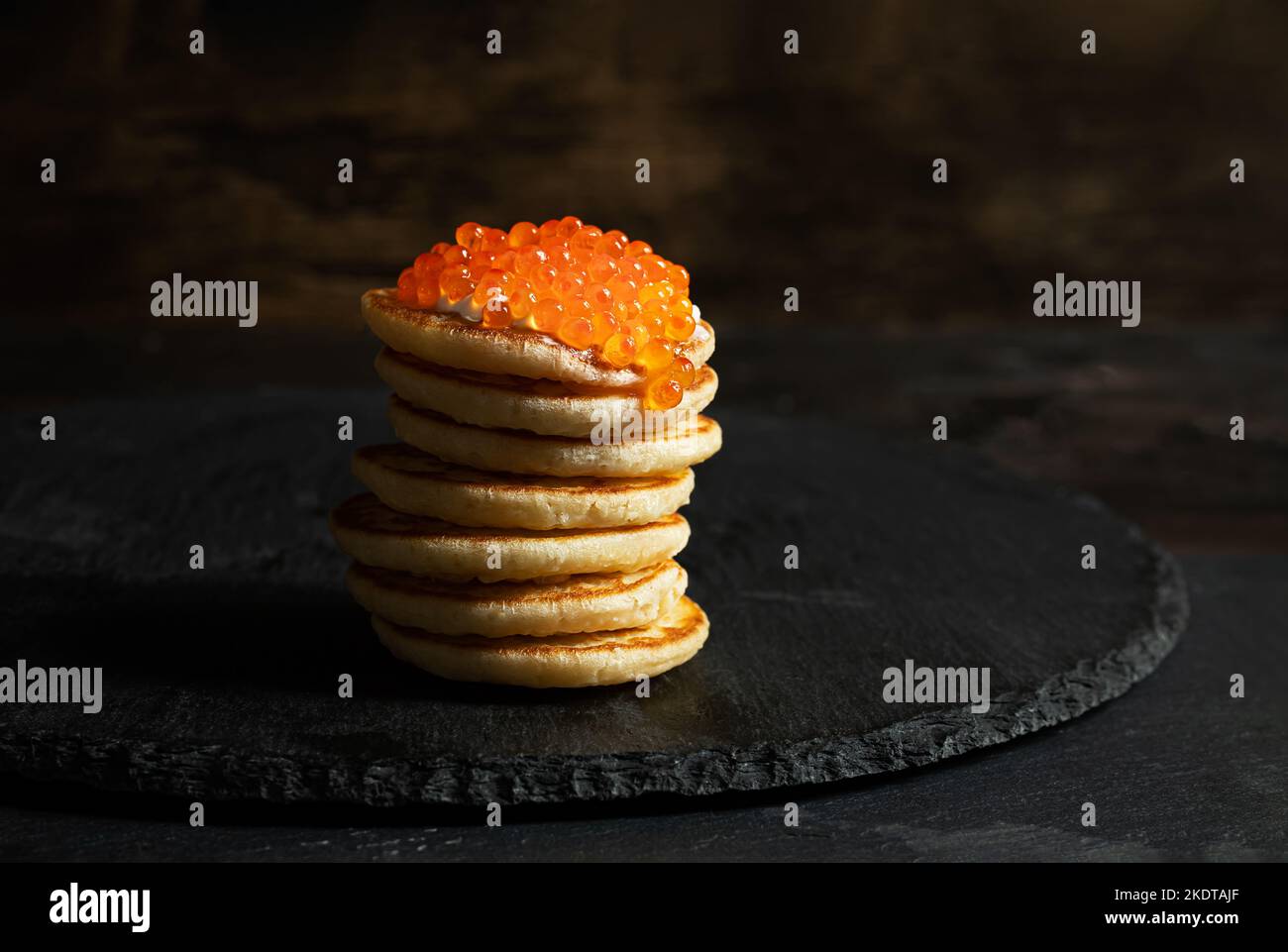 Red caviar on small pancakes blinis with sour cream on dark background Stock Photo