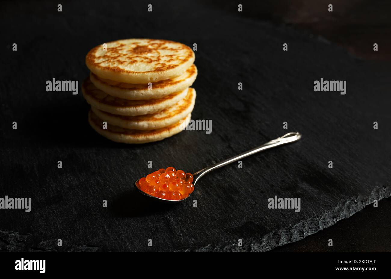 A spoonful of red caviar and small pancakes blinis on a slate Stock Photo