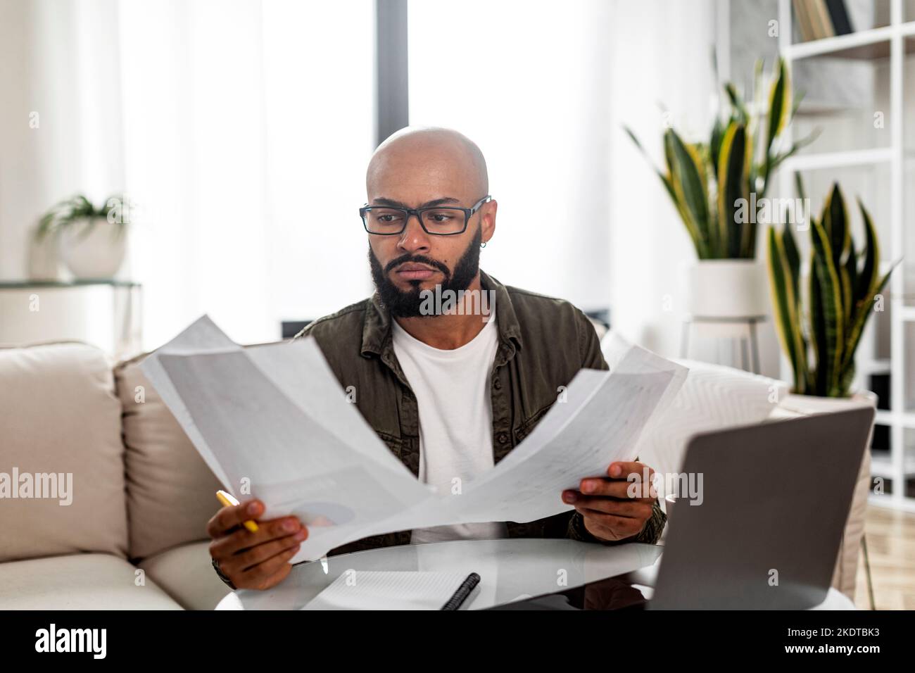 Concentrated mature latin male entrepreneur working with financial documents, checking annual reports and using laptop Stock Photo