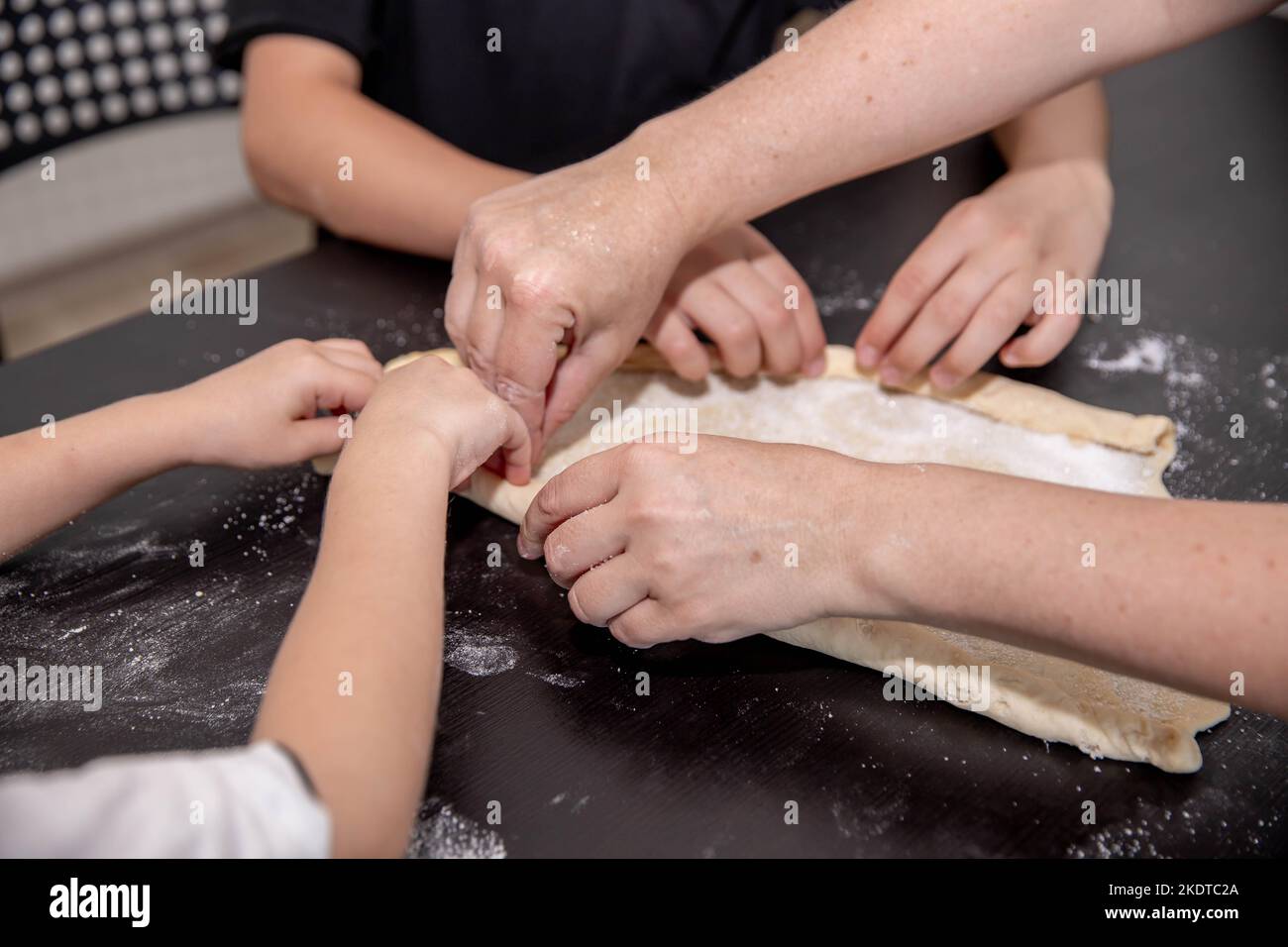 many hands roll out the dough on the slab Stock Photo