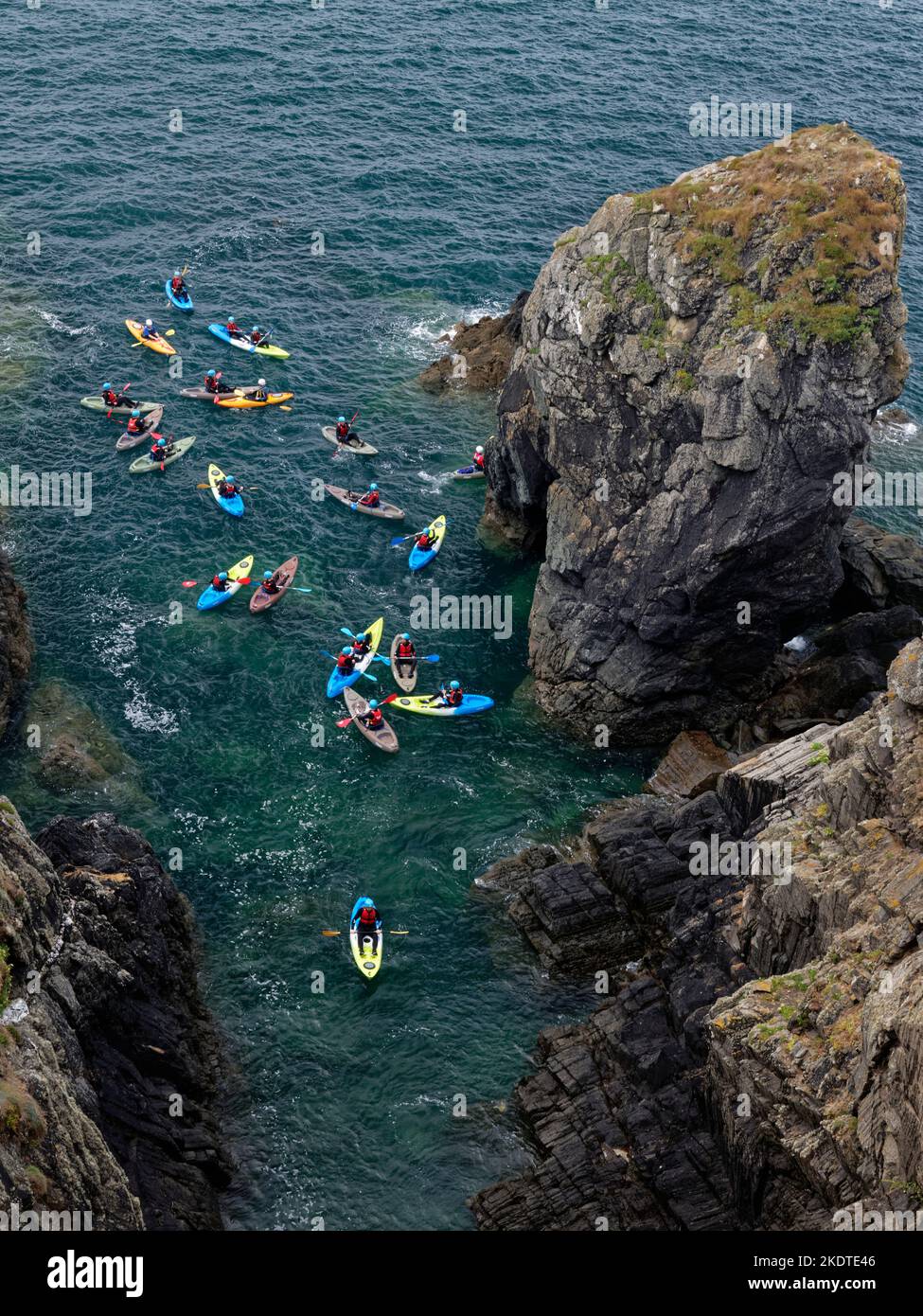 Sea kayakers approaching a natural rock arch as they explore the rugged coastline near Porthclais, St. David’s, Pembrokeshire, Wales, UK, August. Stock Photo