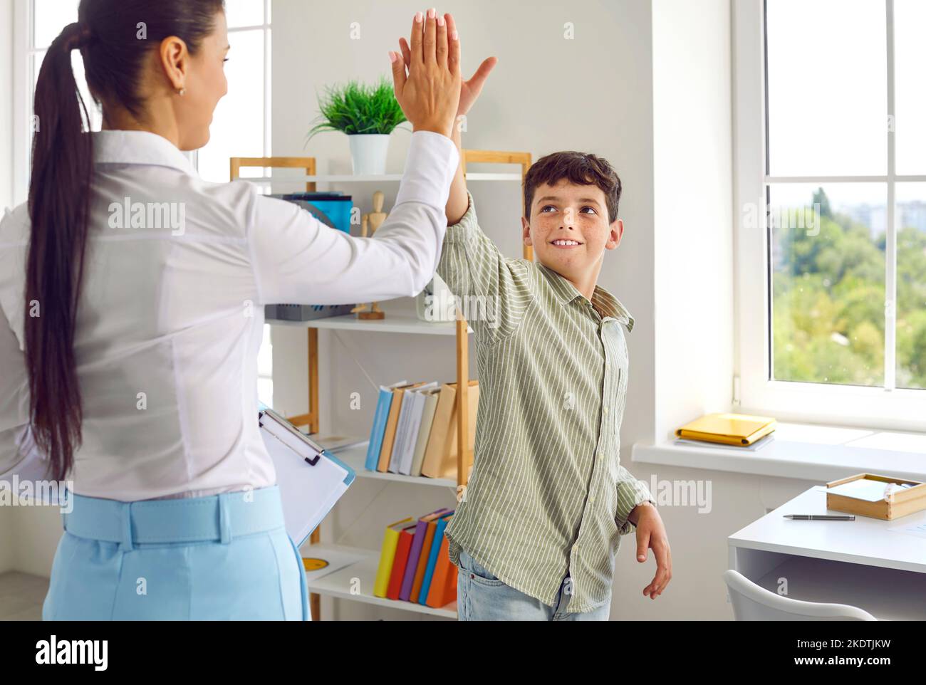 Happy child gives a high five to his therapist or psychologist after successful therapy Stock Photo