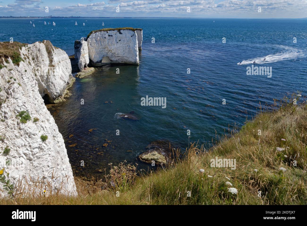 Old Harry’s Rocks with a group of people on jet skis approaching and a sailing regatta in the background in Studland Bay, Studland, Dorset, UK, July. Stock Photo