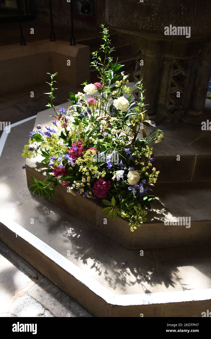 A colourful floral display on the 20th century steps to the font in Hexham Abbey. The font consists of a Roman bowl with a pillar base that has been i Stock Photo