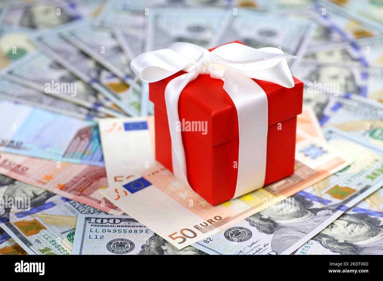 Red gift box wrapped with white ribbon on euro and US dollars background. Romantic surprise for Christmas holidays, New Year in United States and EU Stock Photo