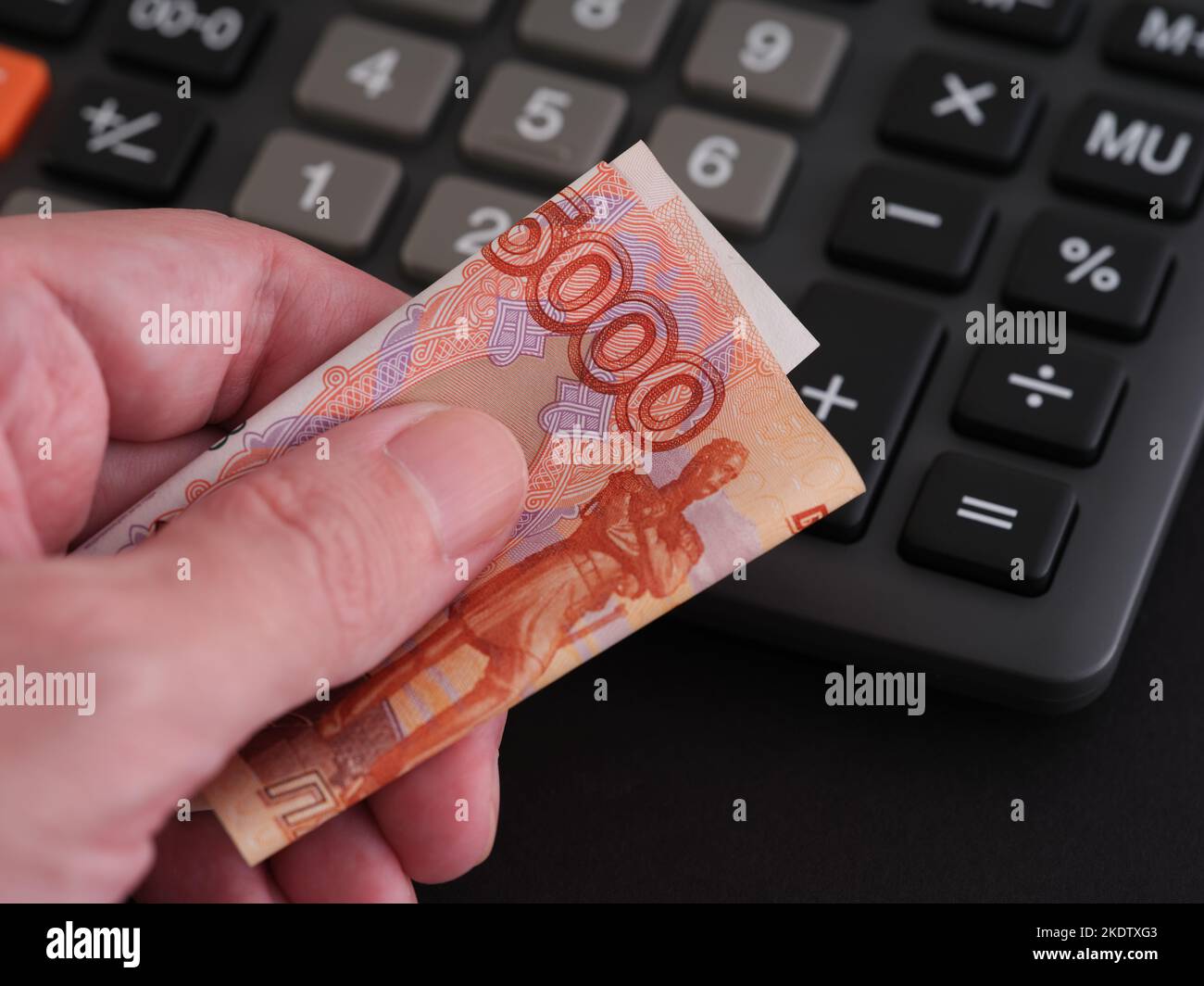 A man holding a five thousand ruble banknote in his hand with a calculator in the background. Close up. Stock Photo