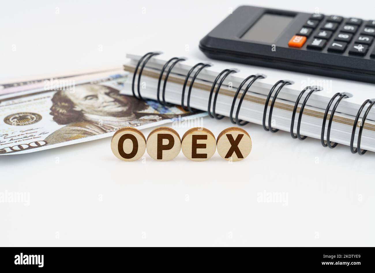 Business concept. On a white surface are dollars, a notebook, a calculator and wooden circles with the inscription - OPEX Stock Photo