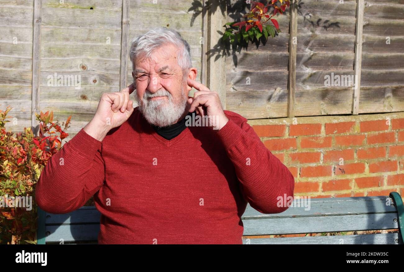 Senior or elderly man with fingers in his ears to stop noise. too loud and ears hurting. Doesn't want to hear what's being said. Stock Photo