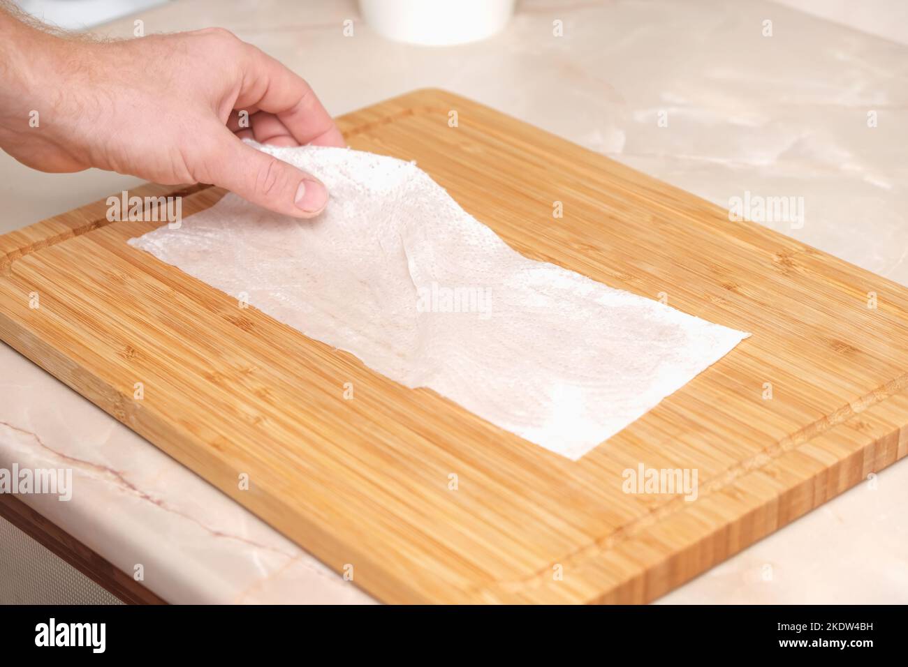 A man wipes a bamboo cutting board with a white paper napkin after