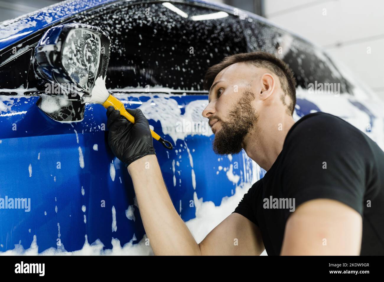 Hand brush washing of car side mirror with foam in car detailing