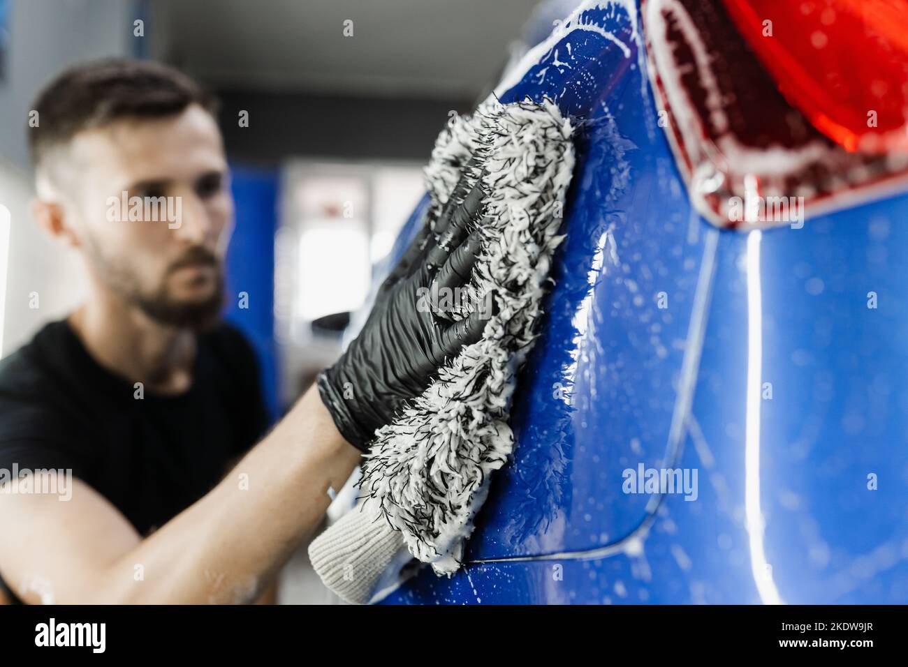 Car washer doing manual foam washing in auto detailing service. Hand washing with microfiber